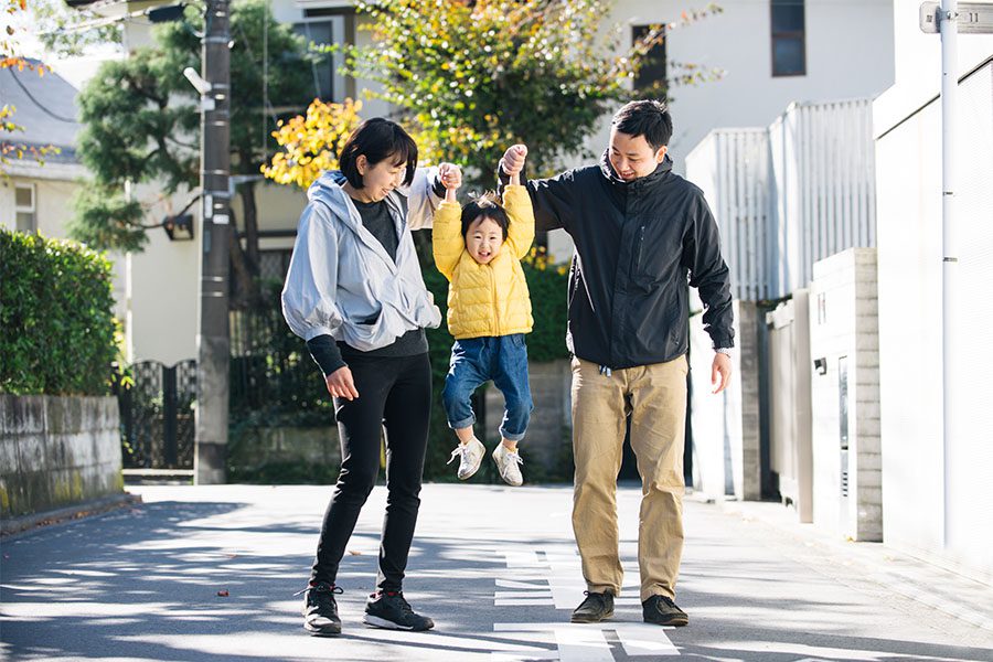 Personal Insurance - Portrait of Two Cheerful Parents Holding Up Their Son in the Air as They Go for a Walk in the Neighborhood on a Sunny Day